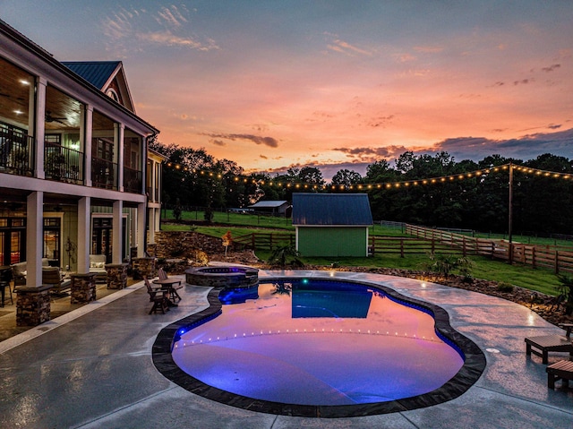 pool at dusk with a shed, a patio, and an in ground hot tub