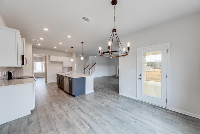 kitchen with hanging light fixtures, white cabinetry, stove, and a center island with sink