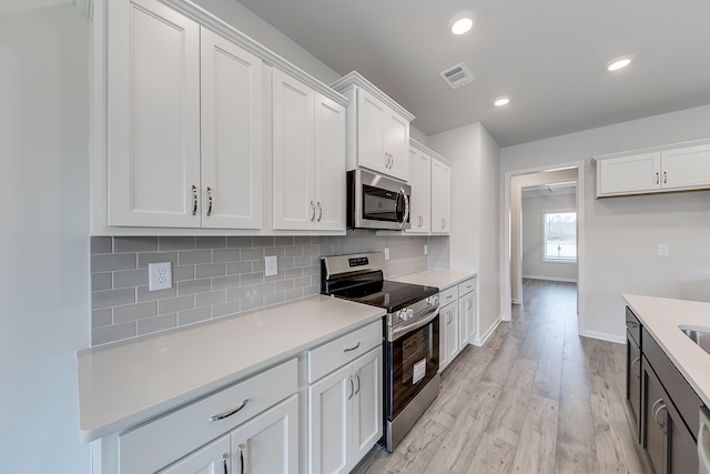 kitchen featuring white cabinetry, appliances with stainless steel finishes, light hardwood / wood-style floors, and backsplash