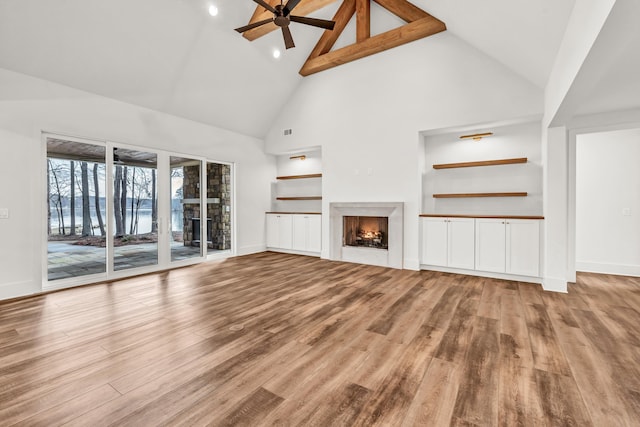 unfurnished living room featuring high vaulted ceiling, wood finished floors, a ceiling fan, built in features, and a lit fireplace
