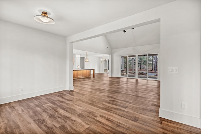 unfurnished living room featuring a chandelier, baseboards, wood finished floors, and vaulted ceiling