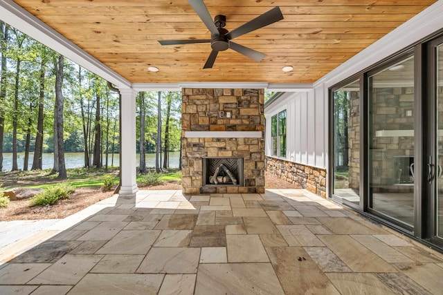 view of patio featuring an outdoor stone fireplace, a water view, ceiling fan, and view of scattered trees