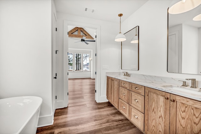 full bath with wood finished floors, double vanity, a freestanding bath, a ceiling fan, and baseboards