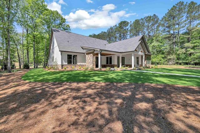 view of front facade with roof with shingles, a front yard, and stone siding