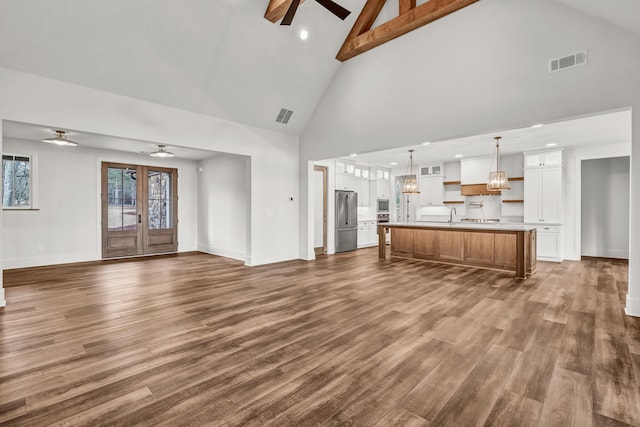 unfurnished living room with ceiling fan, high vaulted ceiling, dark wood-type flooring, a sink, and baseboards