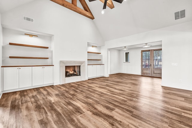unfurnished living room with ceiling fan, high vaulted ceiling, wood finished floors, a premium fireplace, and built in features