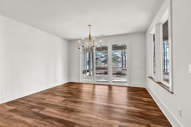 unfurnished dining area featuring a chandelier, dark wood-style flooring, and baseboards