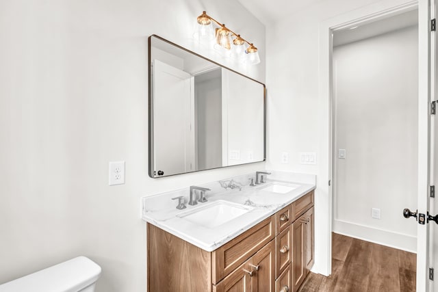 bathroom featuring wood finished floors, toilet, double vanity, and baseboards