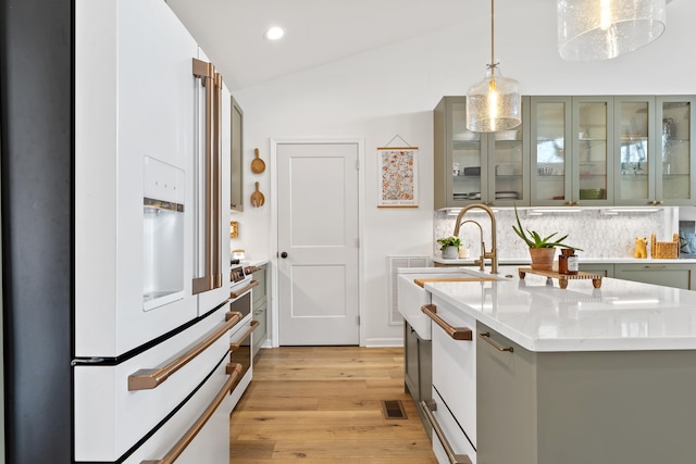 kitchen featuring light countertops, a center island with sink, pendant lighting, high end fridge, and glass insert cabinets