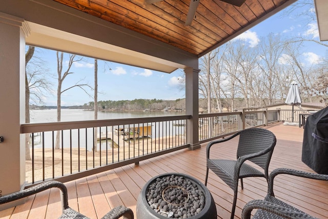 wooden terrace with an outdoor fire pit, a water view, and a ceiling fan