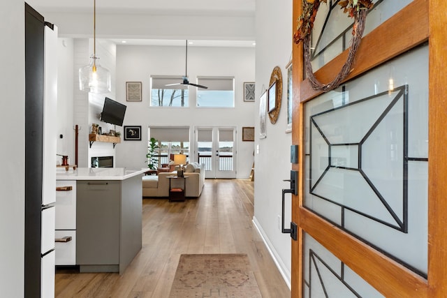 entrance foyer featuring a towering ceiling, french doors, baseboards, light wood-style floors, and ceiling fan