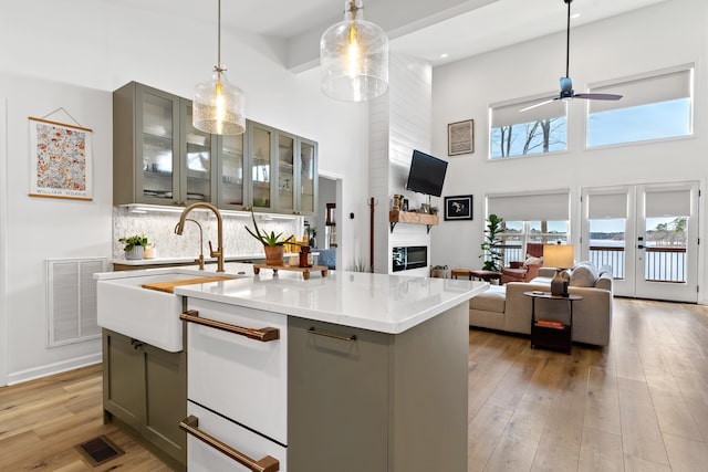 kitchen with visible vents, light wood finished floors, decorative light fixtures, an island with sink, and glass insert cabinets