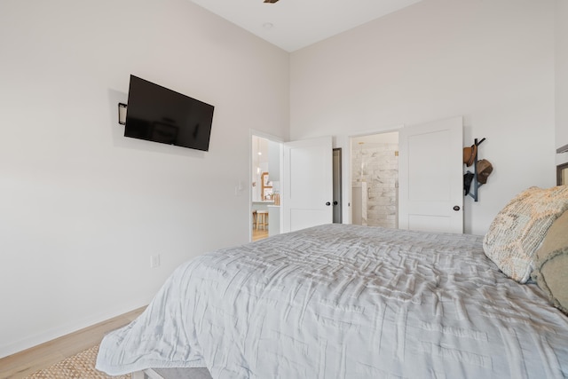 bedroom featuring light wood-type flooring, a towering ceiling, and connected bathroom