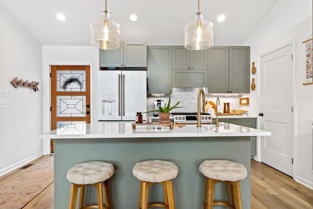 kitchen with a kitchen island with sink, light countertops, white fridge with ice dispenser, tasteful backsplash, and decorative light fixtures