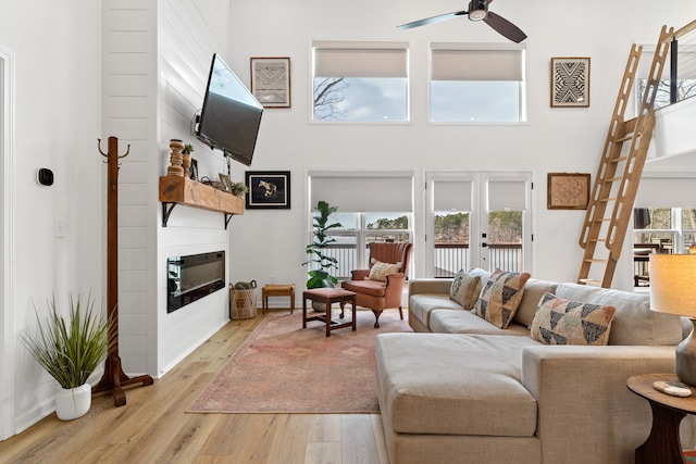 living area with light wood finished floors, french doors, a glass covered fireplace, and a high ceiling