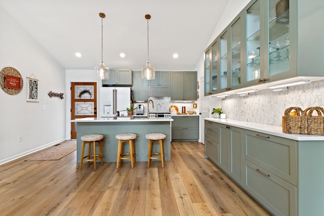 kitchen with hanging light fixtures, light countertops, high end fridge, decorative backsplash, and glass insert cabinets