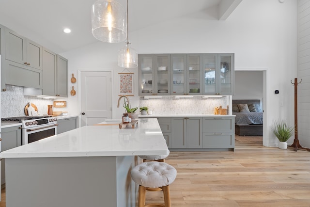 kitchen with lofted ceiling, a kitchen island, glass insert cabinets, high end range, and pendant lighting