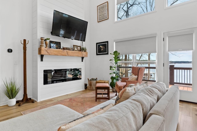 living room featuring a towering ceiling, light wood-style floors, baseboards, and a glass covered fireplace