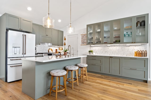 kitchen featuring hanging light fixtures, light countertops, vaulted ceiling, glass insert cabinets, and white fridge with ice dispenser