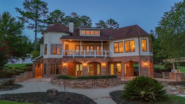 back house at dusk with a balcony and a patio area