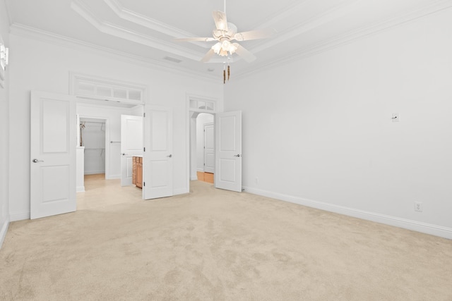 unfurnished bedroom with a spacious closet, a raised ceiling, crown molding, light carpet, and a closet