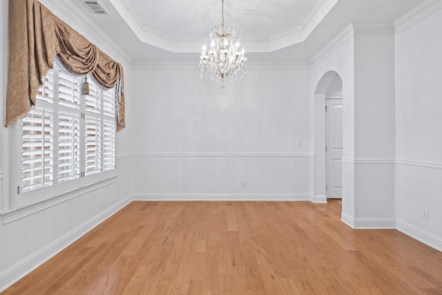 spare room featuring an inviting chandelier, ornamental molding, a raised ceiling, and light hardwood / wood-style flooring