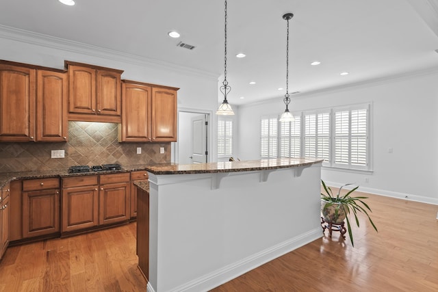 kitchen with stainless steel gas stovetop, a kitchen island, dark stone counters, and decorative light fixtures