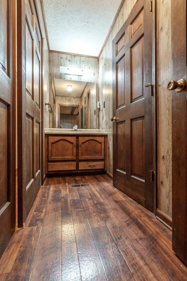 hallway with ornamental molding, wooden walls, a textured ceiling, and dark hardwood / wood-style flooring