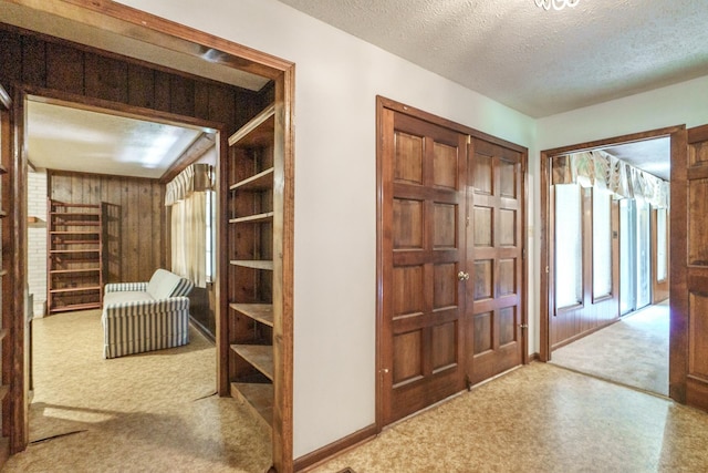 hallway with carpet floors, a textured ceiling, and wood walls