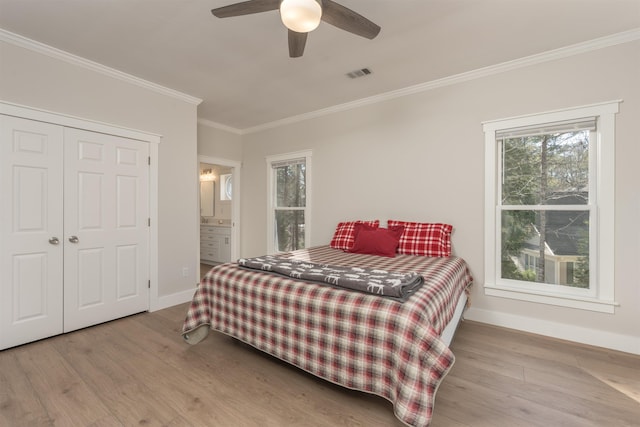 bedroom featuring crown molding, ensuite bath, light wood-type flooring, a closet, and ceiling fan