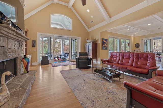 living room featuring beam ceiling, high vaulted ceiling, a stone fireplace, and light hardwood / wood-style floors