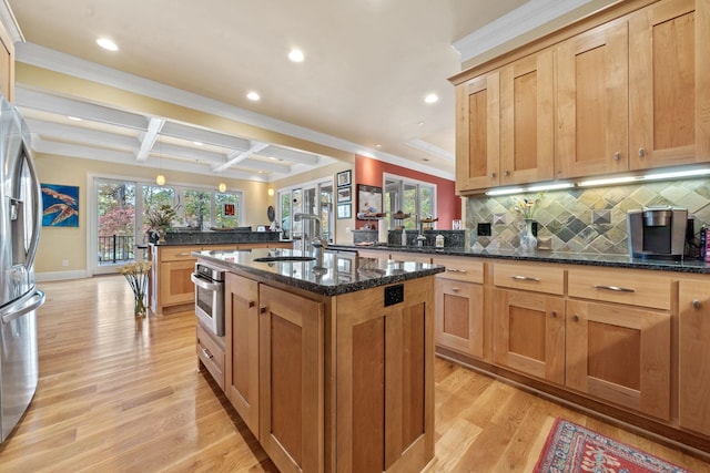 kitchen with appliances with stainless steel finishes, an island with sink, sink, dark stone countertops, and coffered ceiling