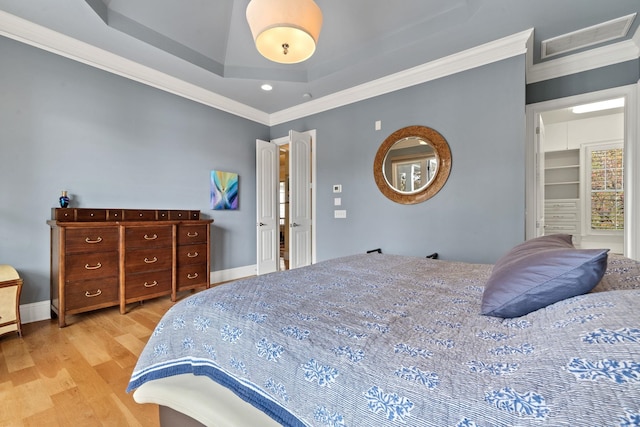 bedroom featuring crown molding, light hardwood / wood-style floors, and a tray ceiling