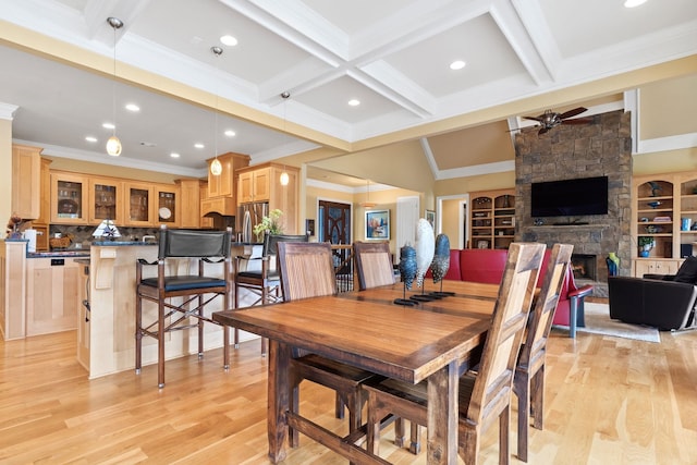 dining room featuring beam ceiling, a stone fireplace, light hardwood / wood-style floors, and ceiling fan