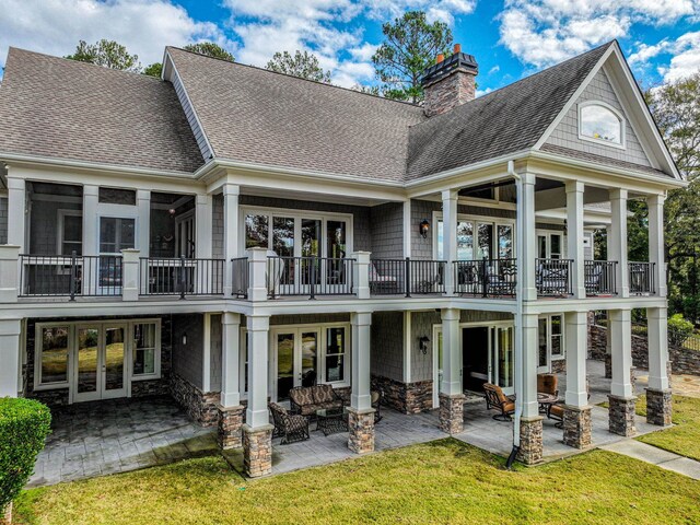 rear view of house with french doors, a balcony, a patio, and a lawn