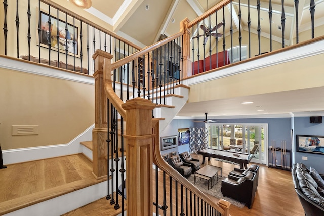 staircase featuring crown molding, a towering ceiling, wood-type flooring, and ceiling fan