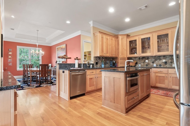 kitchen featuring a kitchen island with sink, light brown cabinetry, decorative light fixtures, and appliances with stainless steel finishes