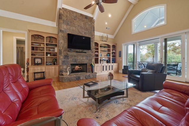 living room featuring built in shelves, a stone fireplace, high vaulted ceiling, light hardwood / wood-style flooring, and ceiling fan