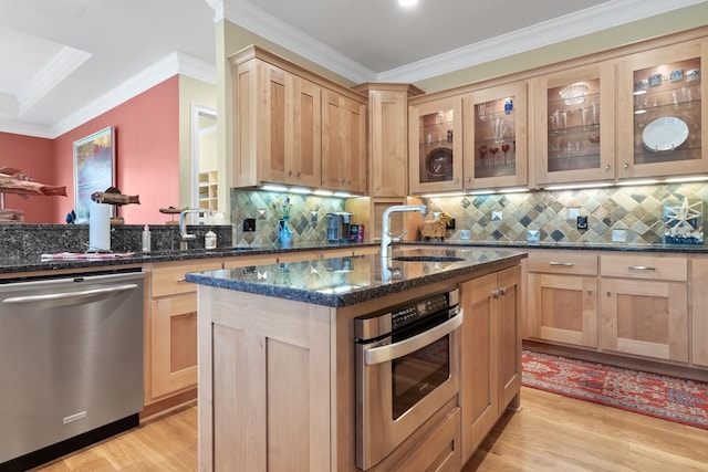 kitchen featuring sink, light hardwood / wood-style flooring, appliances with stainless steel finishes, dark stone countertops, and an island with sink