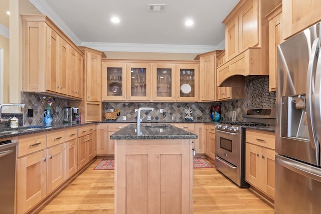 kitchen featuring appliances with stainless steel finishes, sink, dark stone countertops, light brown cabinets, and a center island with sink