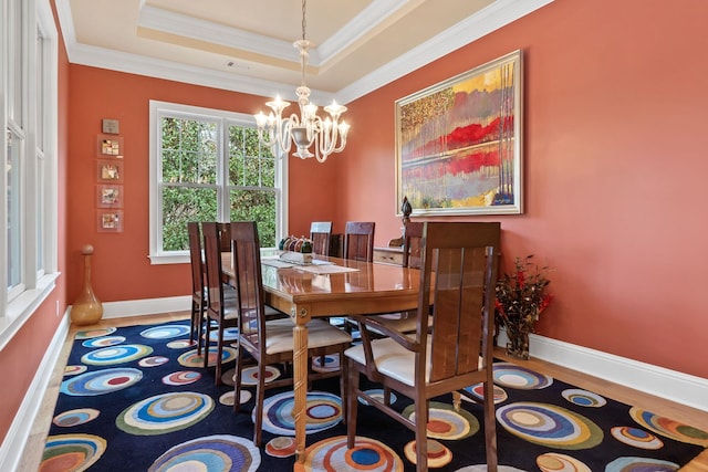 dining area featuring an inviting chandelier, wood-type flooring, crown molding, and a raised ceiling