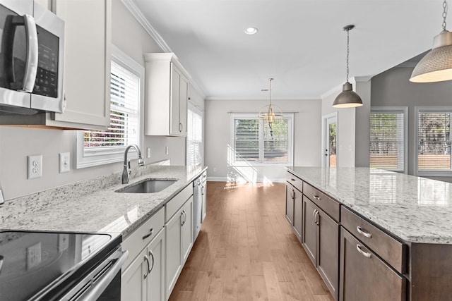 kitchen featuring appliances with stainless steel finishes, a sink, light wood-style floors, white cabinetry, and baseboards