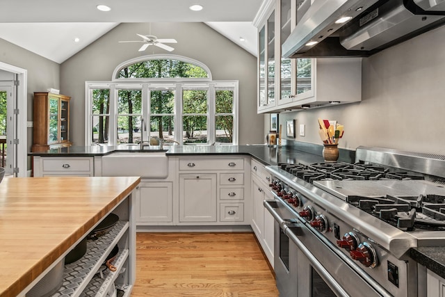 kitchen featuring double oven range, wall chimney exhaust hood, vaulted ceiling, ceiling fan, and light wood finished floors