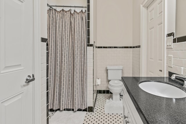 bathroom with tile walls, toilet, curtained shower, wainscoting, and vanity