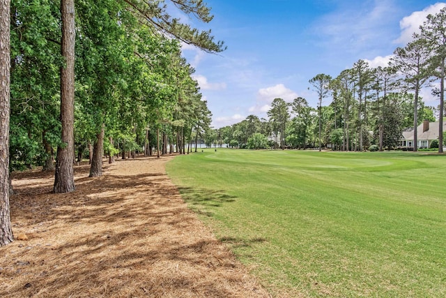 view of property's community with golf course view, a yard, and view of wooded area