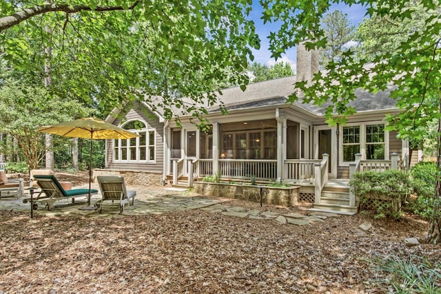 back of house with a sunroom, a chimney, a shingled roof, and a patio area
