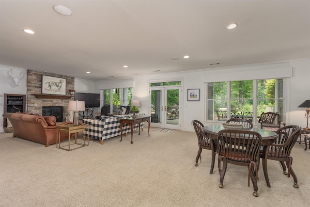 dining room featuring crown molding, a stone fireplace, and light colored carpet