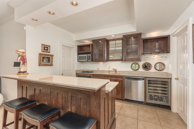 bar featuring sink, light tile patterned floors, appliances with stainless steel finishes, dark brown cabinets, and beverage cooler