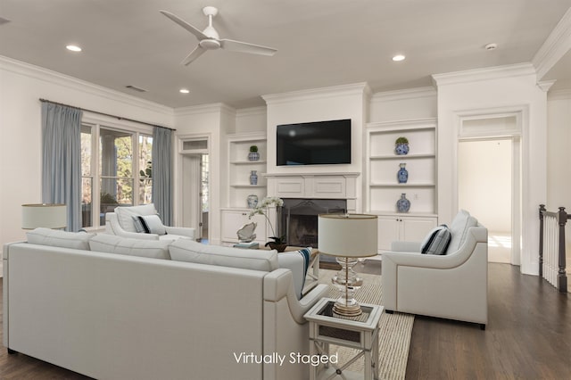 living room featuring built in features, a fireplace, dark hardwood / wood-style flooring, ornamental molding, and ceiling fan