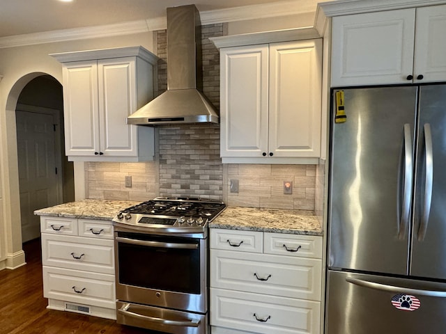 kitchen with dark wood-style floors, ornamental molding, appliances with stainless steel finishes, wall chimney exhaust hood, and tasteful backsplash